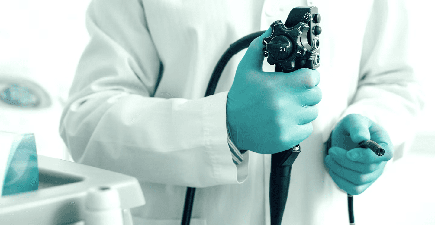Medical professional in blue gloves holding an endoscope control handle and flexible insertion tube tip.