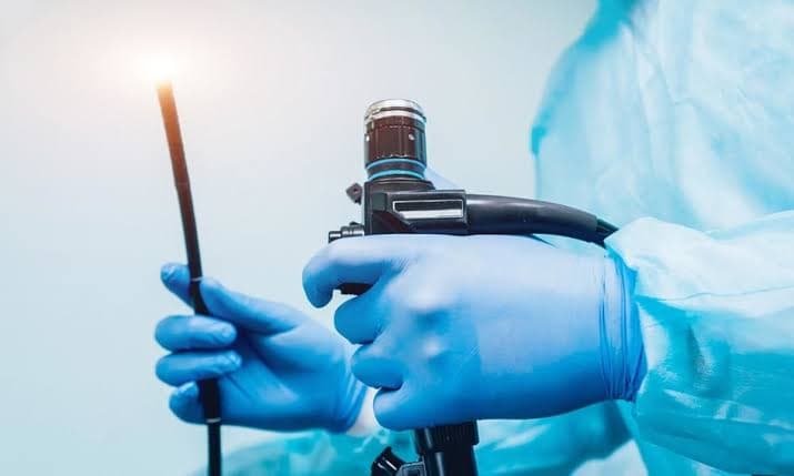 Medical professional in blue gloves holding an endoscope with a bright light at the tip.